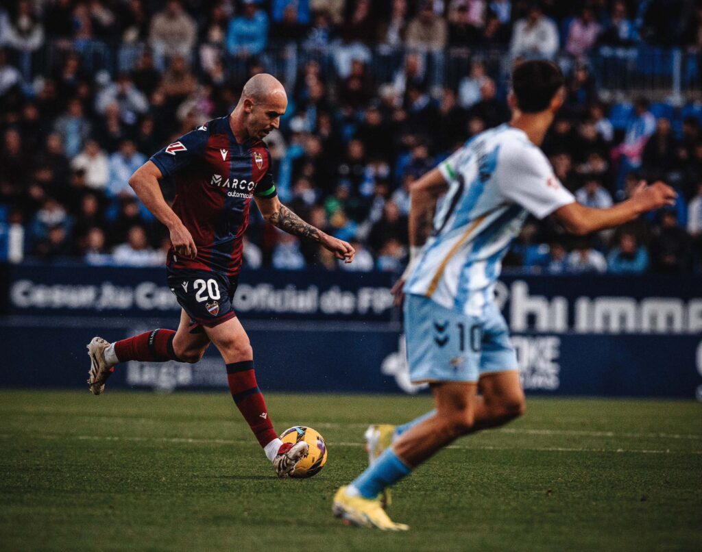 Rey, jugador del Levante UD; y Larrubia, jugador del Málaga CF, en pleno partido de fútbol.